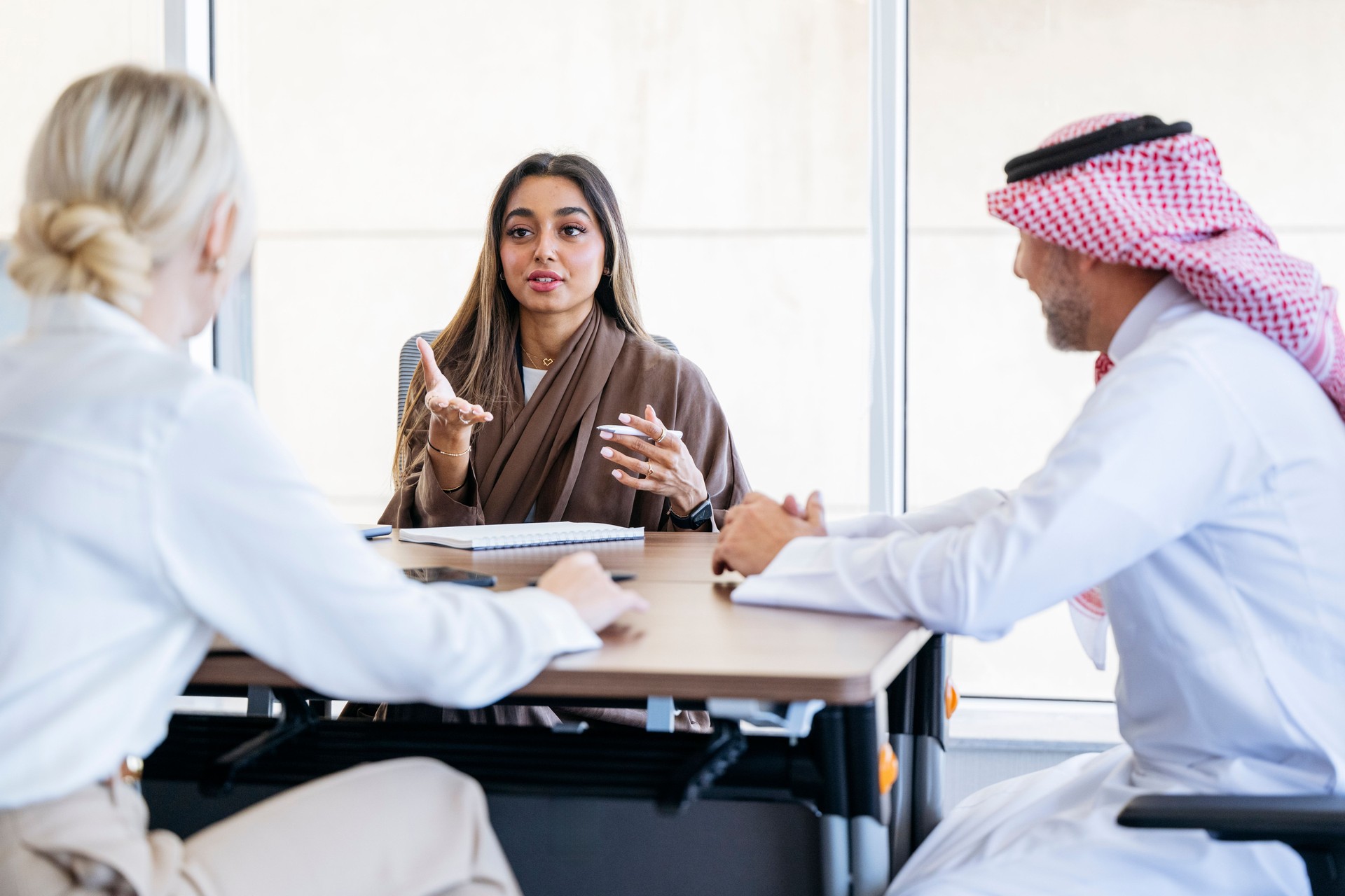 Businesswoman in her 20s talking to colleagues sitting at desk in modern office